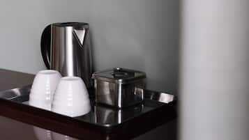 A stainless steel coffee maker, two white cups, and a container on a wooden tray.