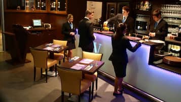Zona de bar con barra, taburetes y un área de estar con mesas y sillas.