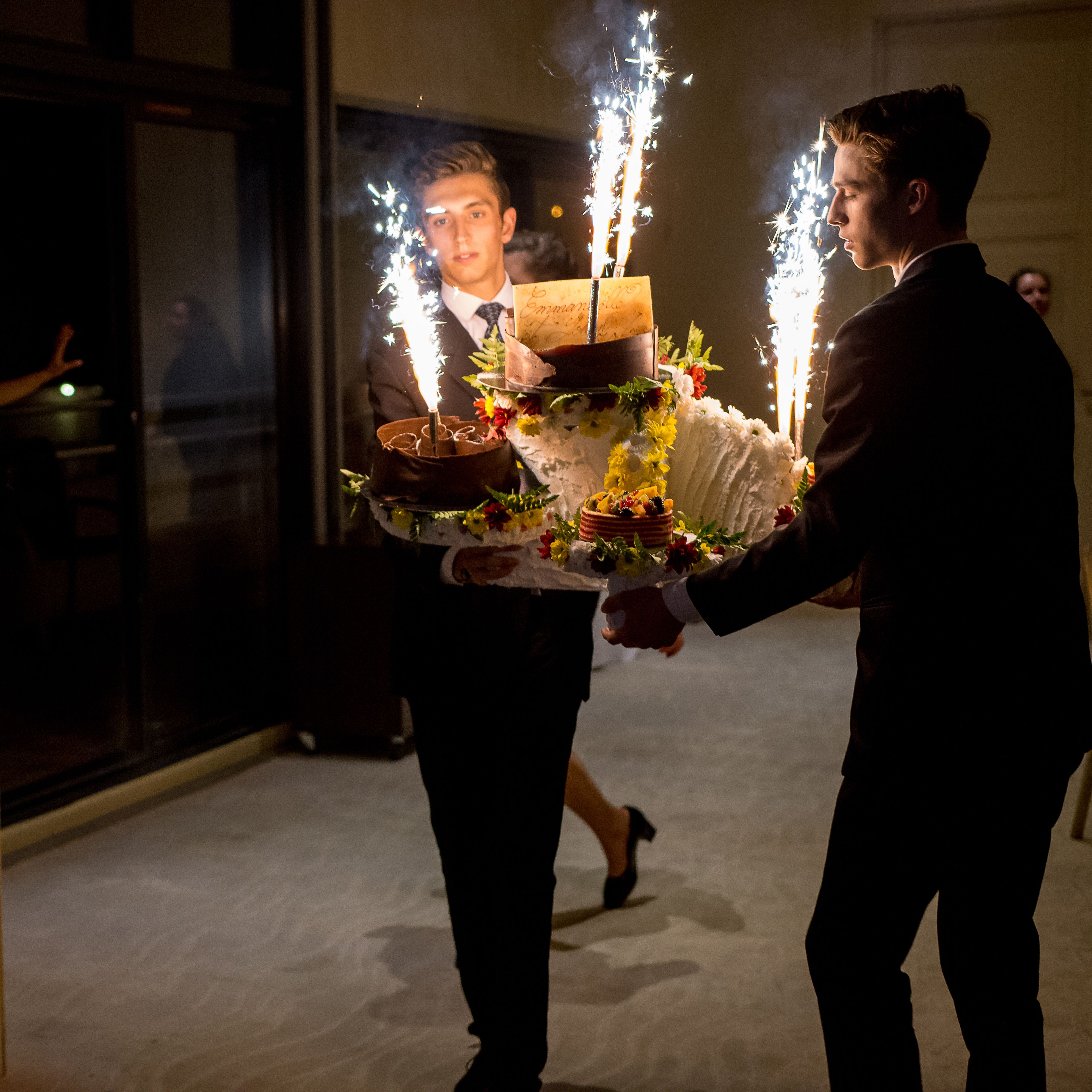 A person holding a cake with sparklers, a cake with a chocolate layer, and a cake with a white layer.