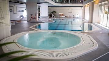 An indoor swimming pool with a hot tub, surrounded by a tiled floor and a white, textured border.