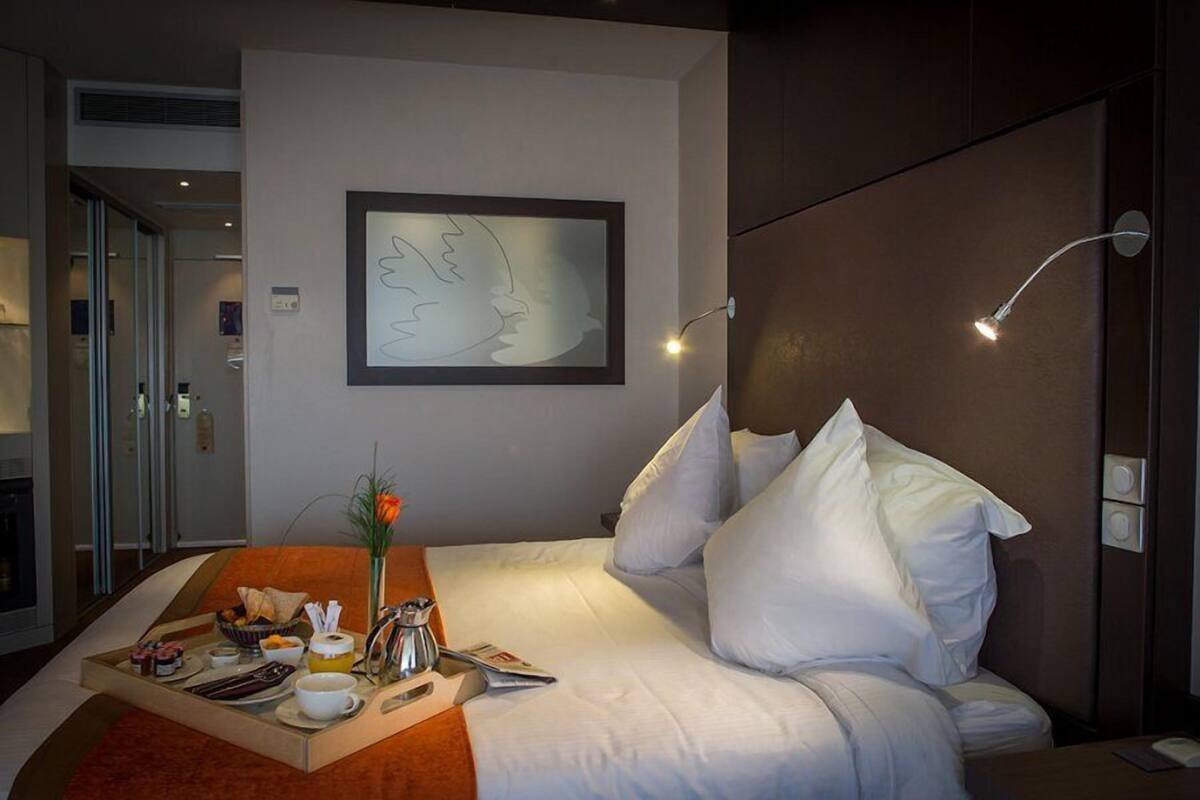 Una habitación de hotel con una cama, una bandeja de desayuno, una obra de arte enmarcada y una lámpara de noche.