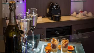 Un coin bar avec une table en verre où sont présentés divers amuse-gueules, une bouteille de vin et des verres.