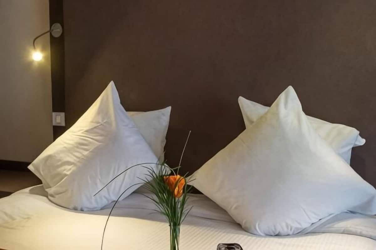 Una cama con almohadas blancas y un jarrón con una flor naranja.