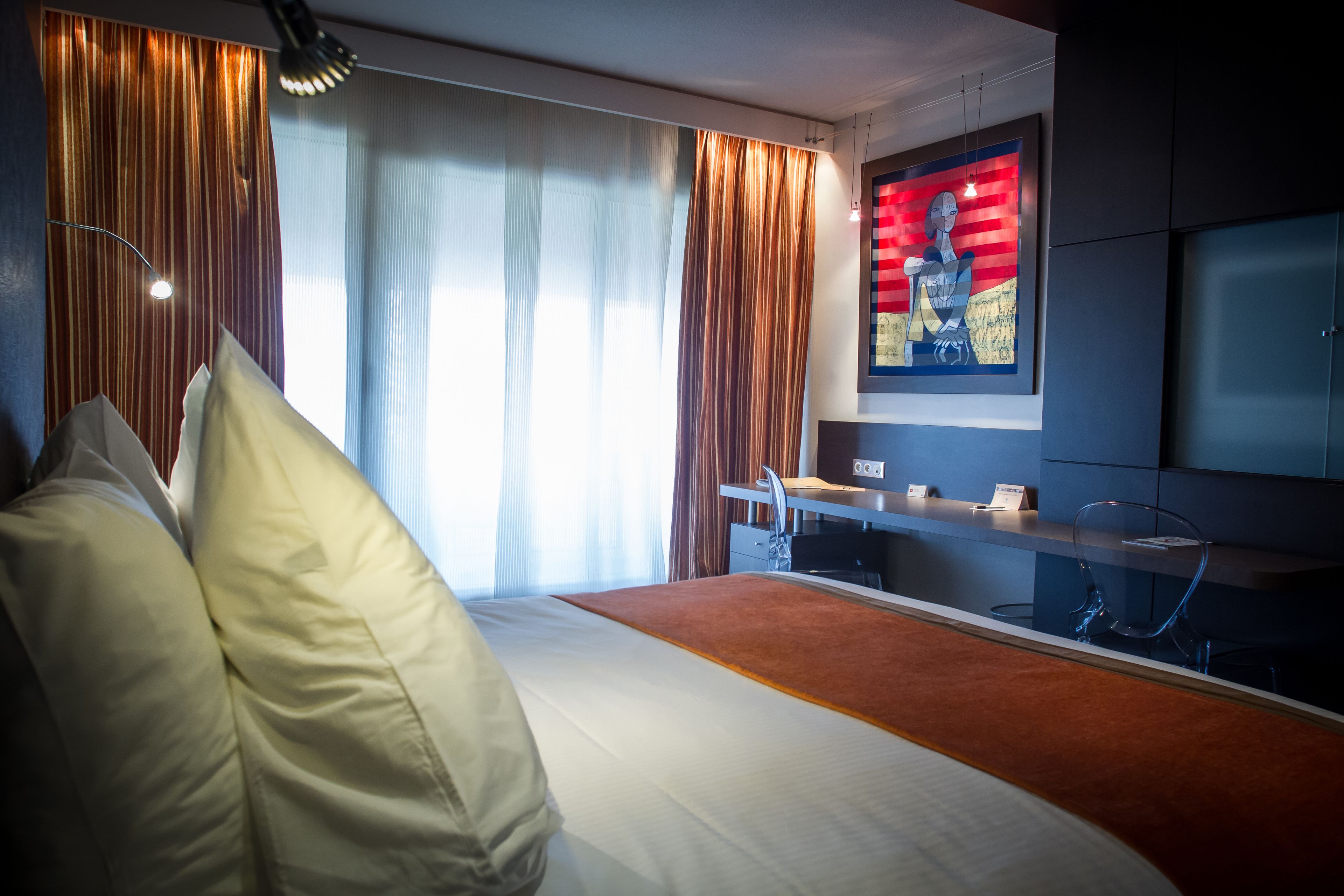 Una habitación de hotel con cama, escritorio, silla, televisor y un cuadro en la pared.