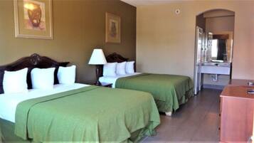A hotel room with two single beds, a nightstand, a lamp, a mirror, and a wooden dresser.