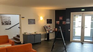 A lobby with a staircase, orange seating, a display stand, and a door with a glass panel. - Logis Hôtel & Restaurant & Bar LE COTTAGE (Calais)