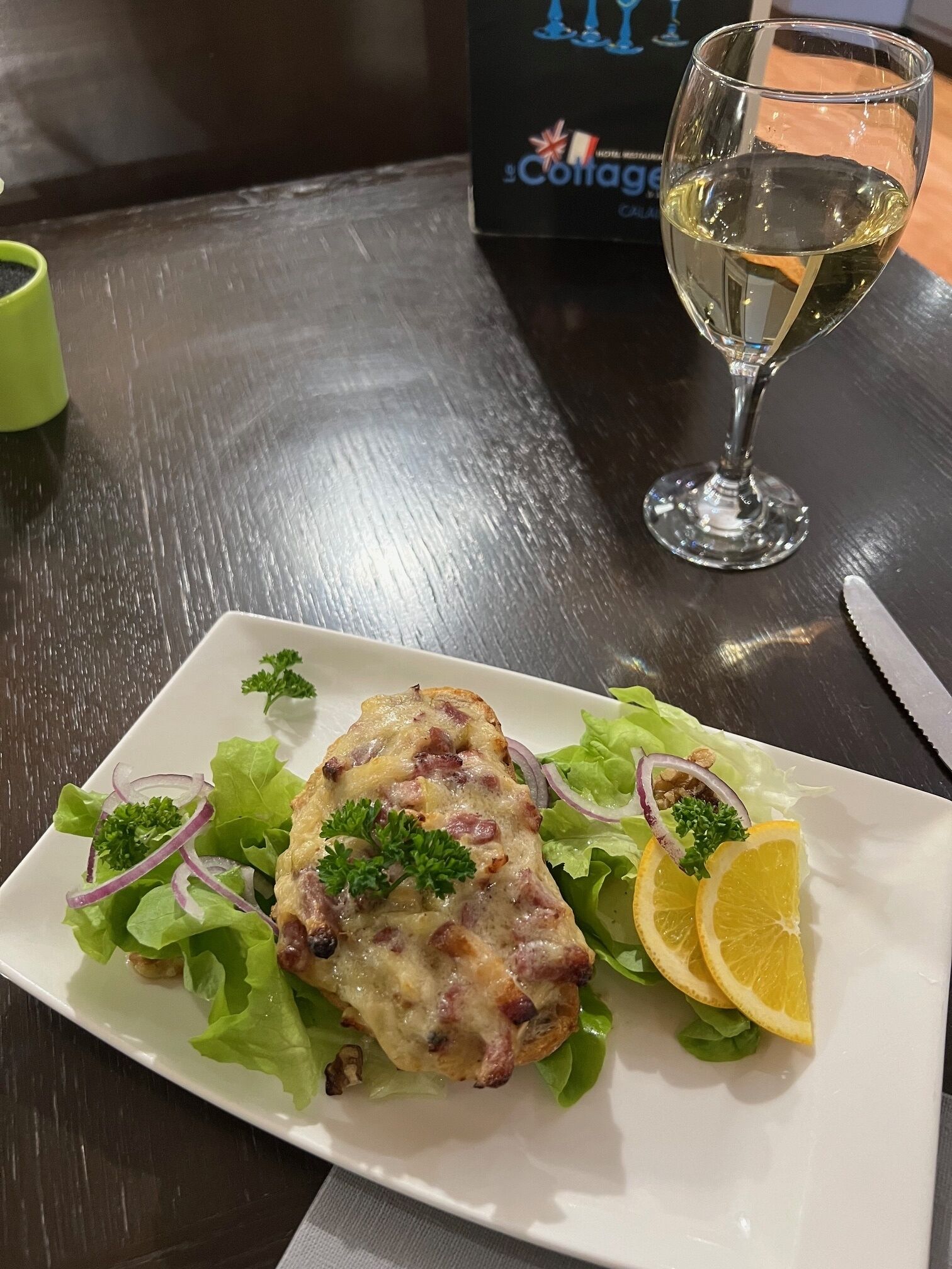 Un plato de comida con una copa de vino blanco sobre una mesa de madera.