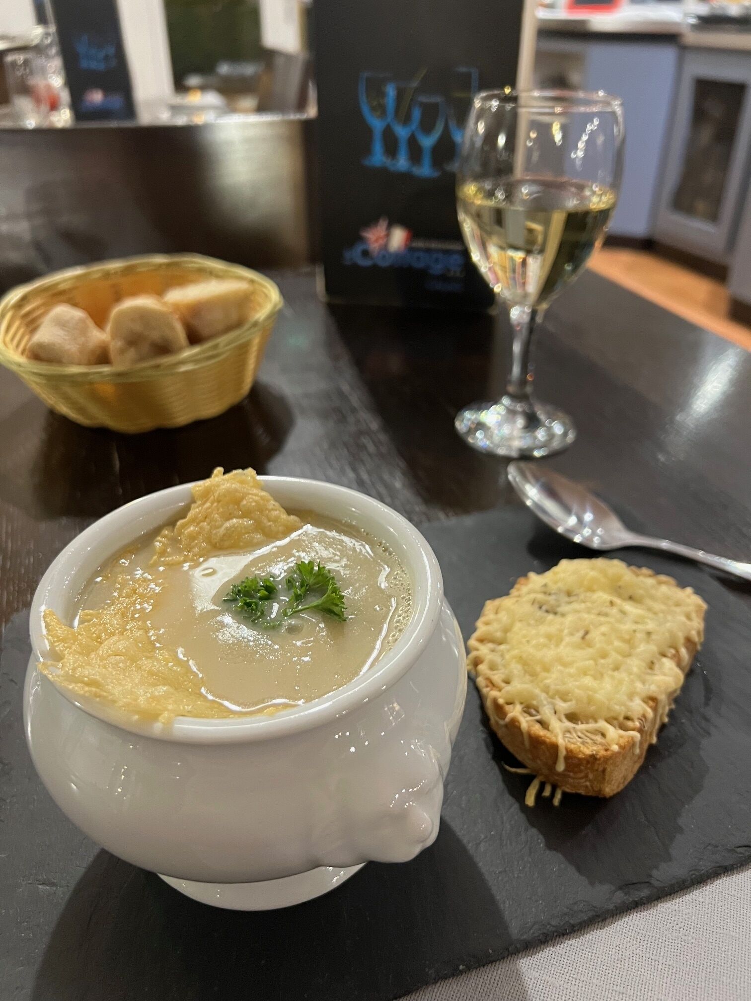 Una ciotola di zuppa guarnita, una fetta di pane e un bicchiere di vino bianco su un tavolo.