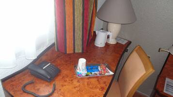 Hotelkamer met bureau, telefoon, lamp, stoel en een klein tafeltje met toiletartikelen.