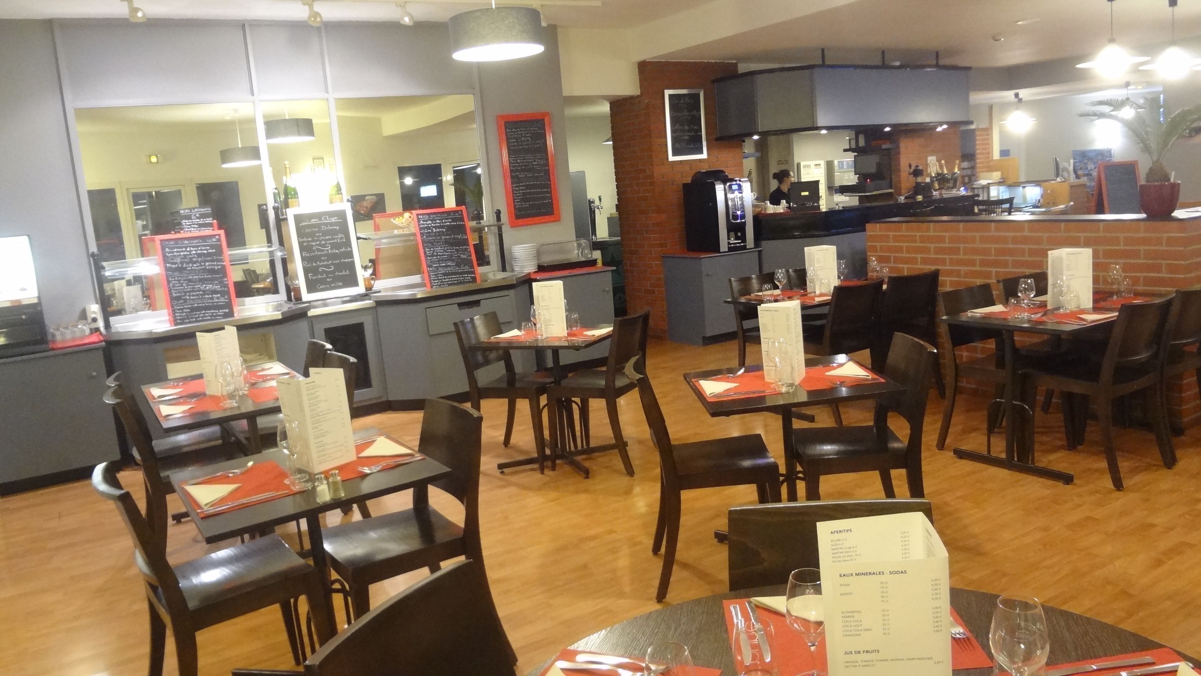 A restaurant interior with multiple tables and chairs, a counter with a menu, and a kitchen area in the background.