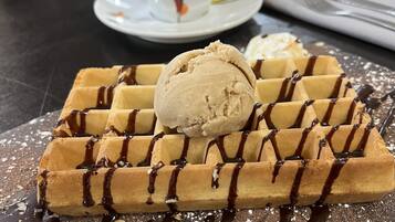 A waffle with chocolate drizzle and a scoop of ice cream on a wooden board.