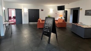 A spacious lobby with a blackboard displaying event information, dark tiled flooring, and orange seating areas. - Logis Hôtel & Restaurant & Bar LE COTTAGE (Calais)