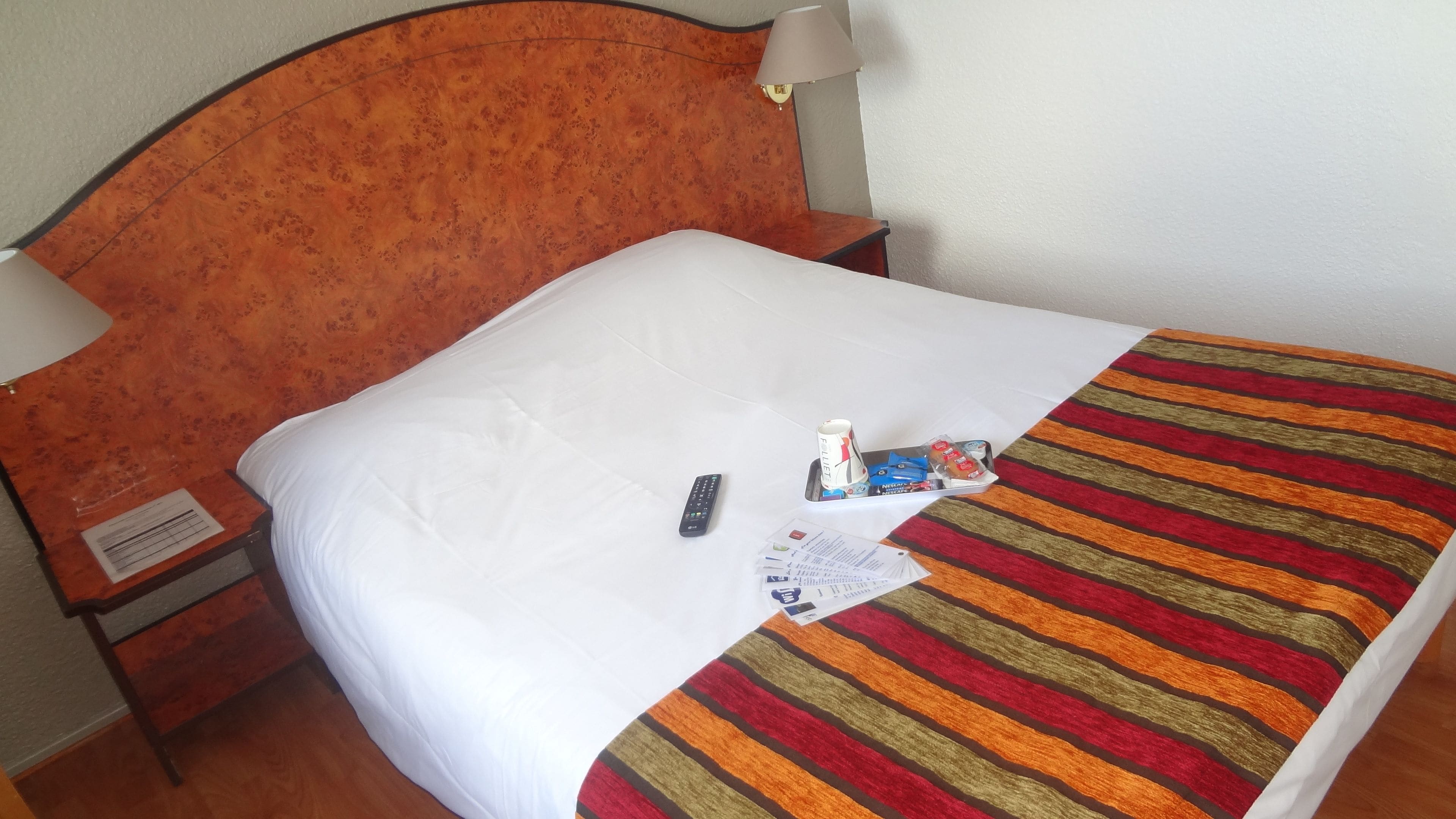 A neatly made bed with a striped blanket, a remote control, and some toiletries on the bed.