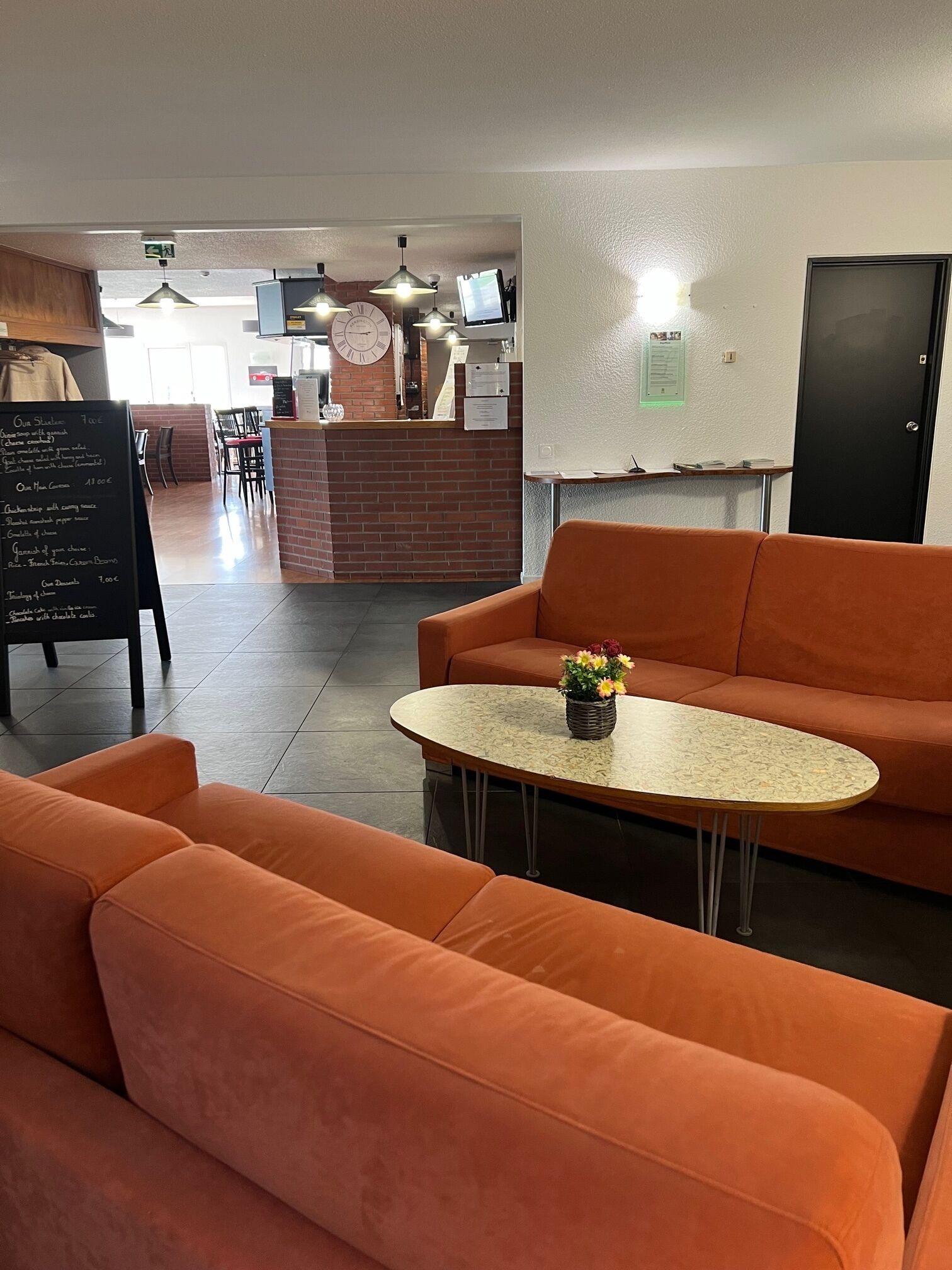 Un hall d'entrée moderne avec des sièges orange, un comptoir d'accueil et un panneau affichant le menu.