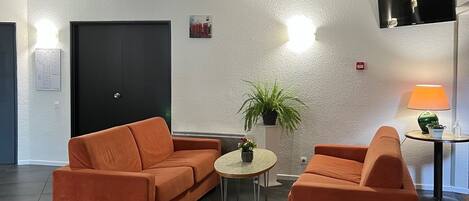 A modern living room with two orange sofas, a small round table with a plant, and a flat-screen TV mounted on the wall.