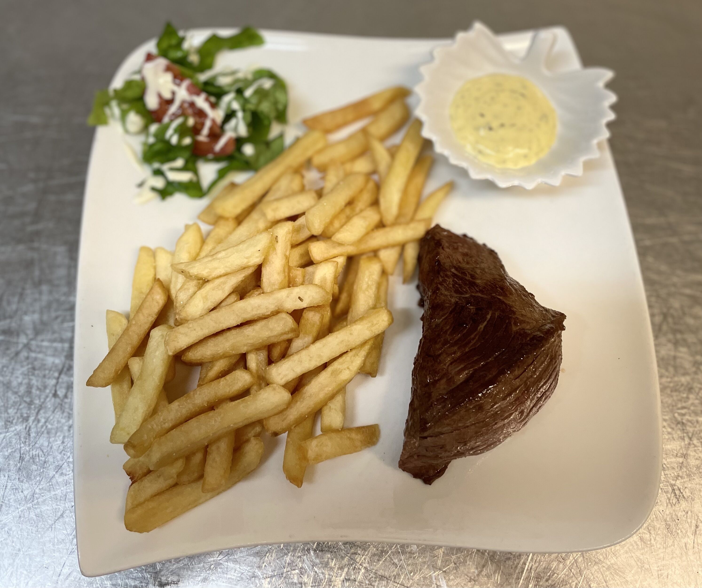 A plate with French fries, a piece of meat, and a salad with a creamy sauce.