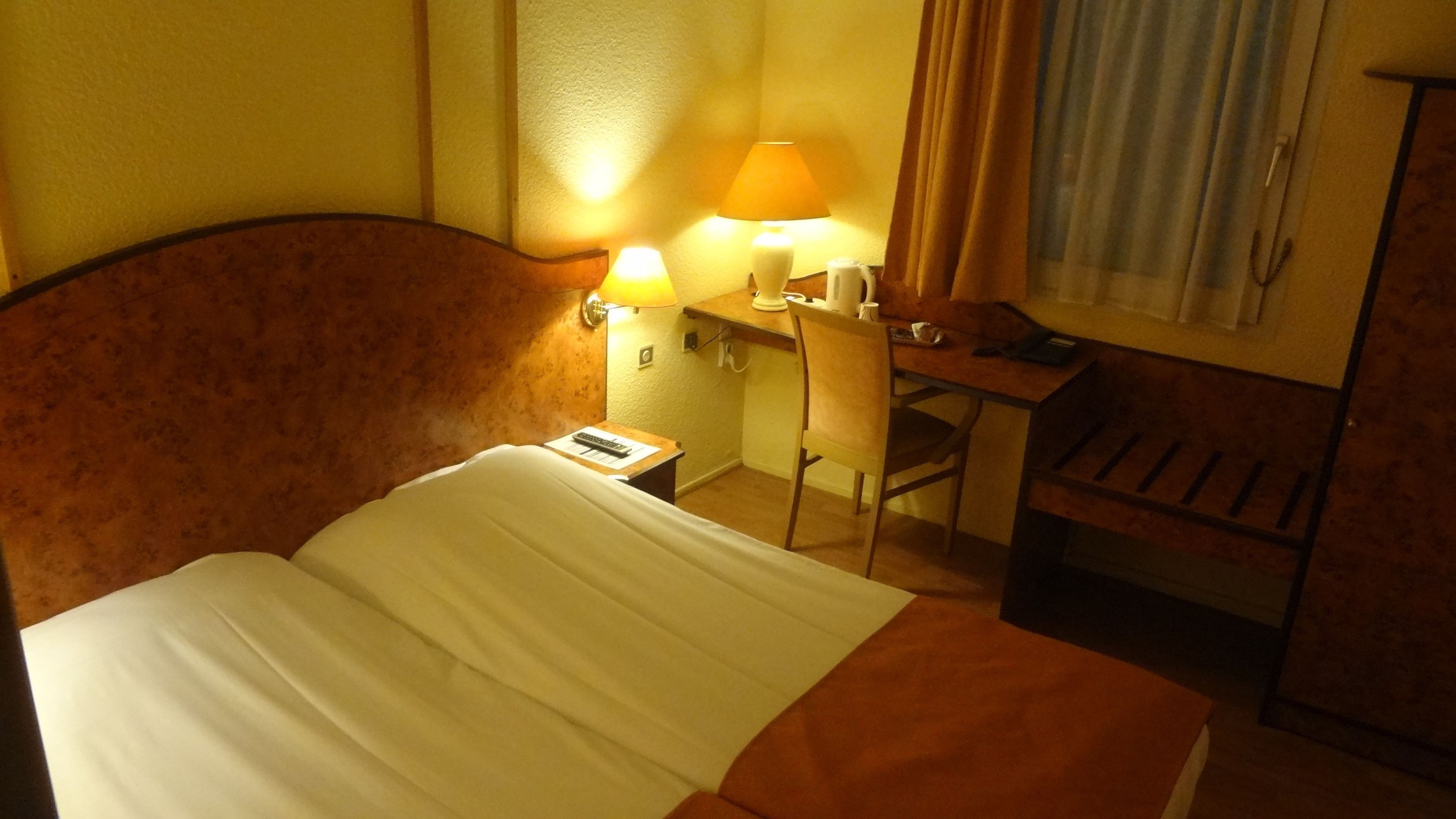 A hotel room with a bed, a desk, a chair, and two lamps.