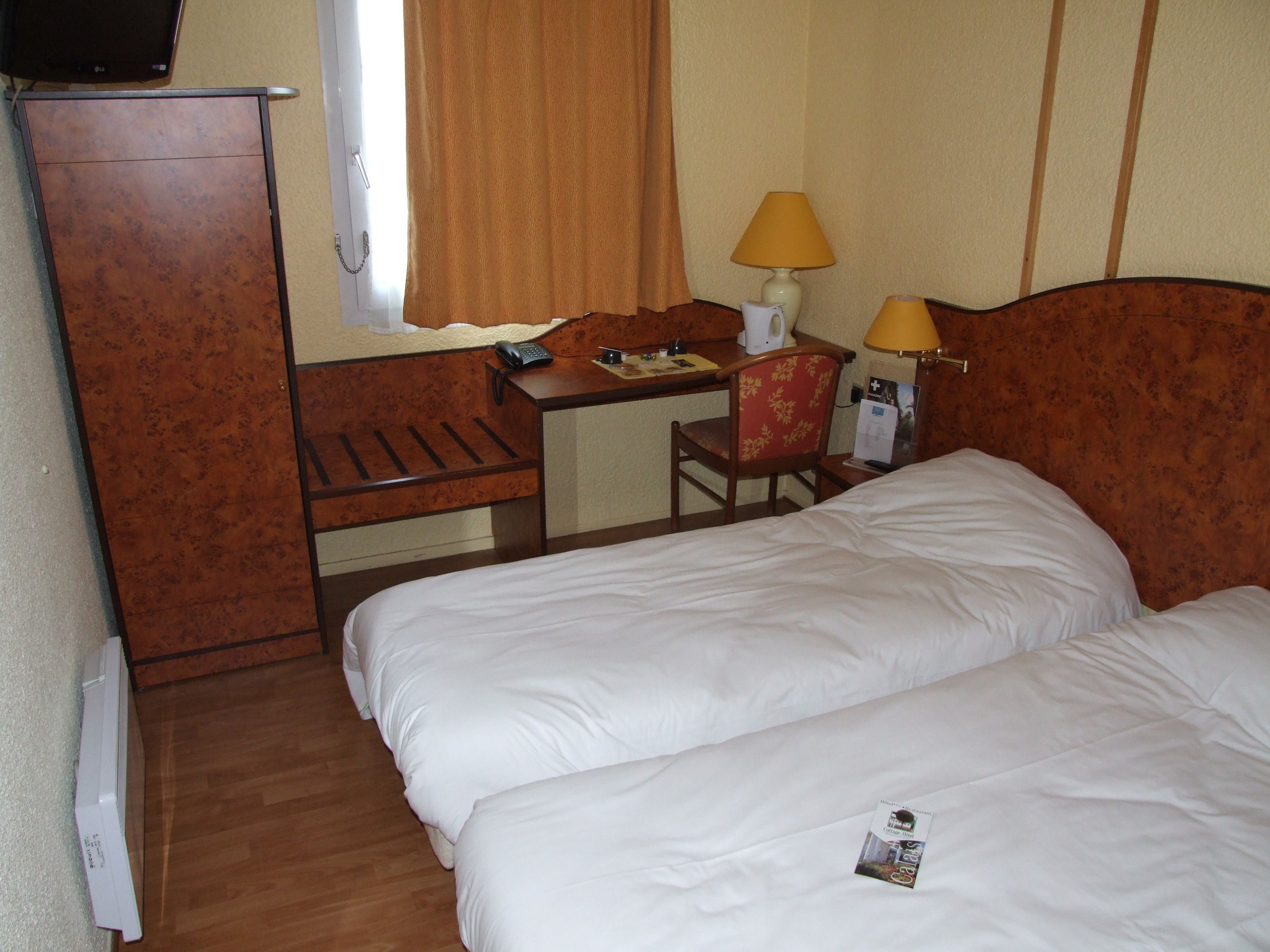 Ein Hotelzimmer mit zwei Betten, einem Schreibtisch, einem Stuhl, einer Lampe und einem Fernseher.