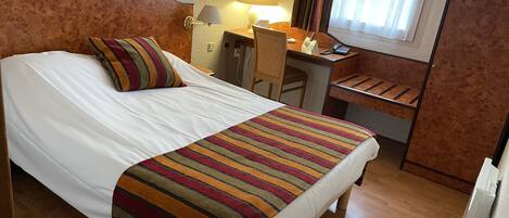 Una habitación de hotel con cama, escritorio, silla y lámpara.