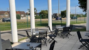 An outdoor patio area with tables and chairs, surrounded by white columns, under a clear blue sky. - Logis Hôtel & Restaurant & Bar LE COTTAGE (Calais)