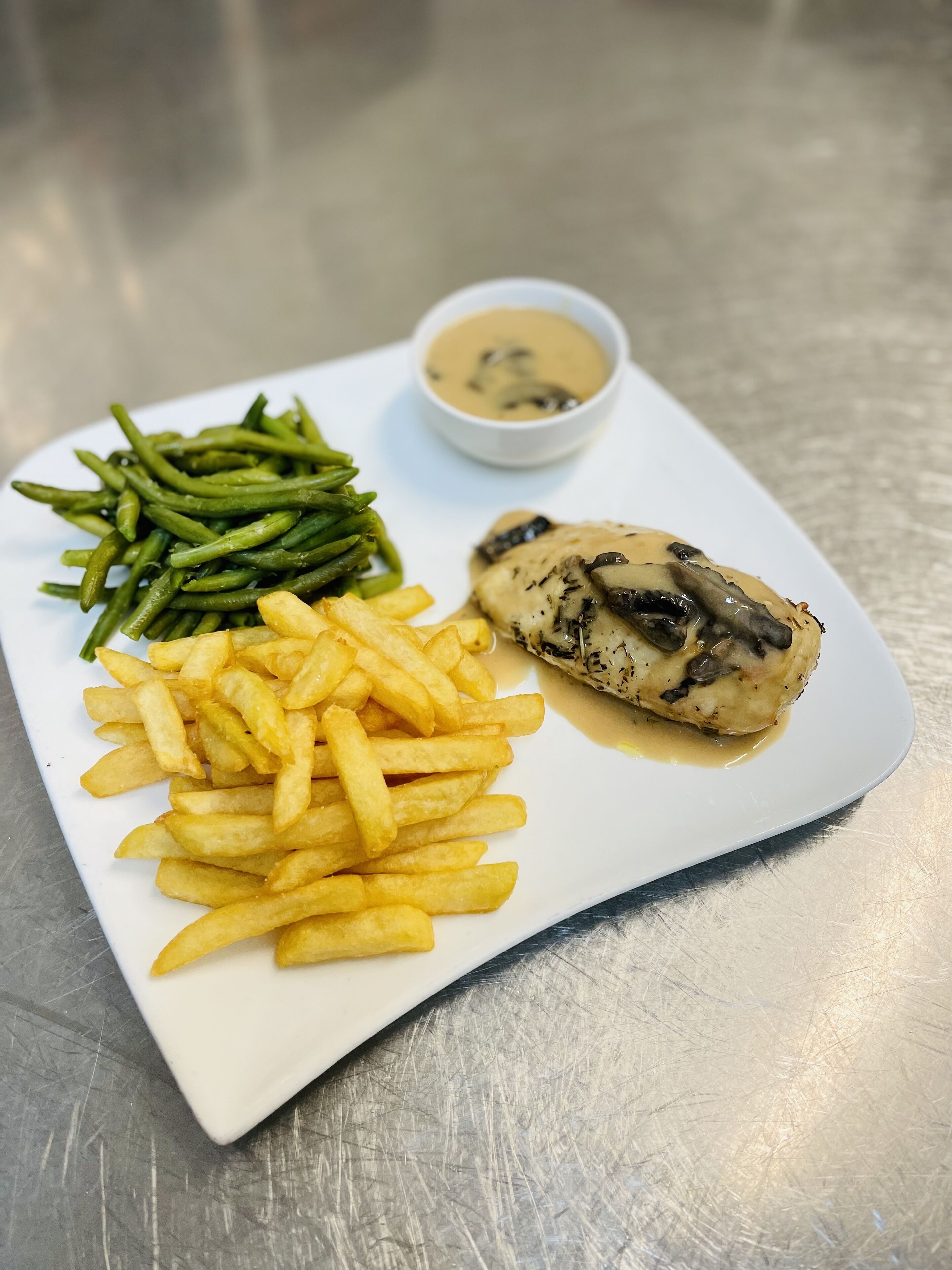 Une assiette contenant un morceau de poulet, des haricots verts et des frites.