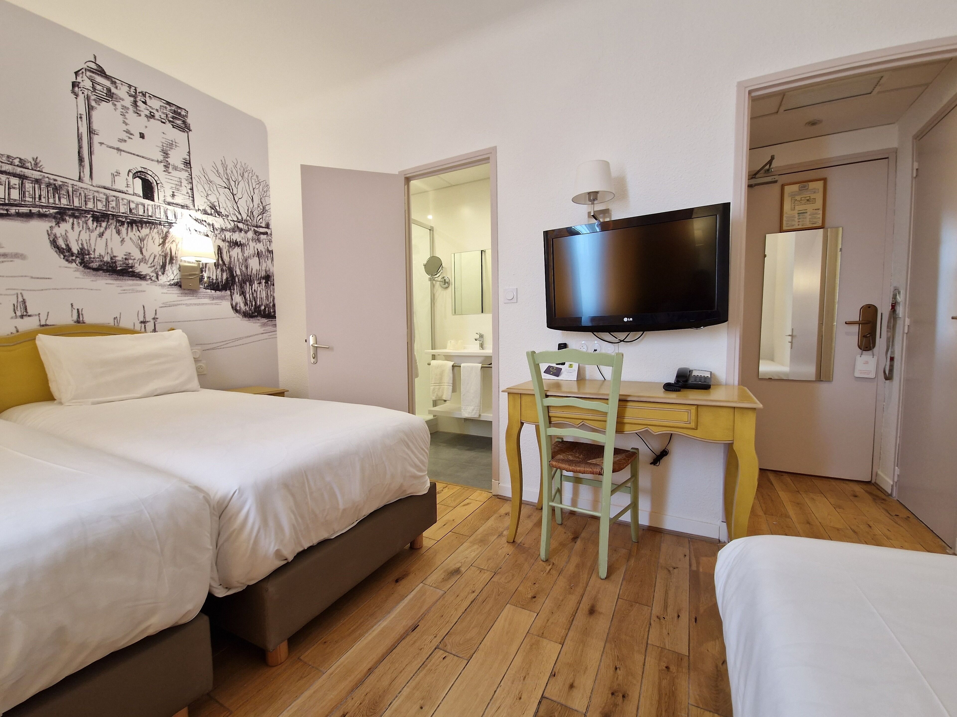 Habitación de hotel con cama, escritorio con silla, televisión y baño visible a través de una puerta abierta.