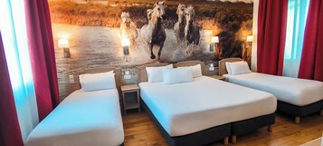 Habitación de hotel con dos camas individuales, piso de madera, un gran mural en la pared con caballos y una cortina roja.