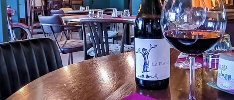 Interior de un restaurante con mesas, sillas, luces colgantes, una botella de vino y una copa de vino tinto sobre un plato con comida.