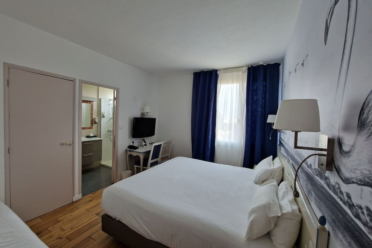 Habitación de hotel con cama, escritorio, televisión y baño visible a través de una puerta abierta.