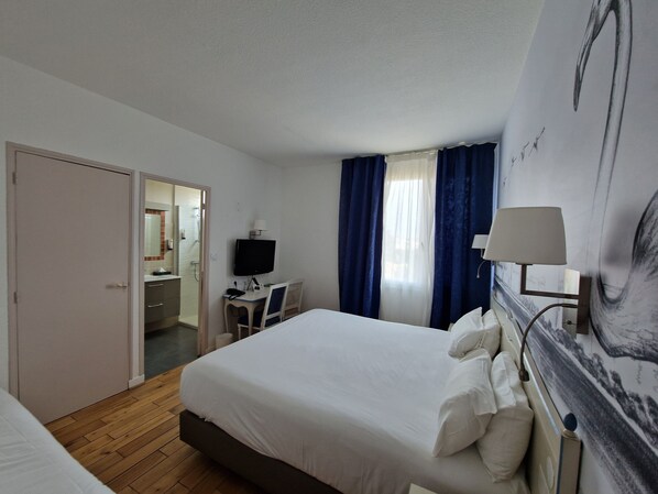 Une chambre d’hôtel avec un lit, un bureau, une télévision et une salle de bain visible à travers une porte ouverte.