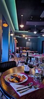 A restaurant interior with tables set for dining, a bottle of wine, and a plate of food.