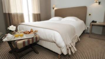 Habitación de hotel con una cama grande, lámparas de noche, una mesita de noche con un teléfono y una bandeja de desayuno con croissants y jugo de naranja.