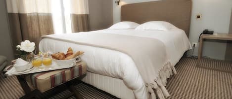 A hotel room with a large bed, bedside lamps, a bedside table with a phone, and a breakfast tray with croissants and orange juice.