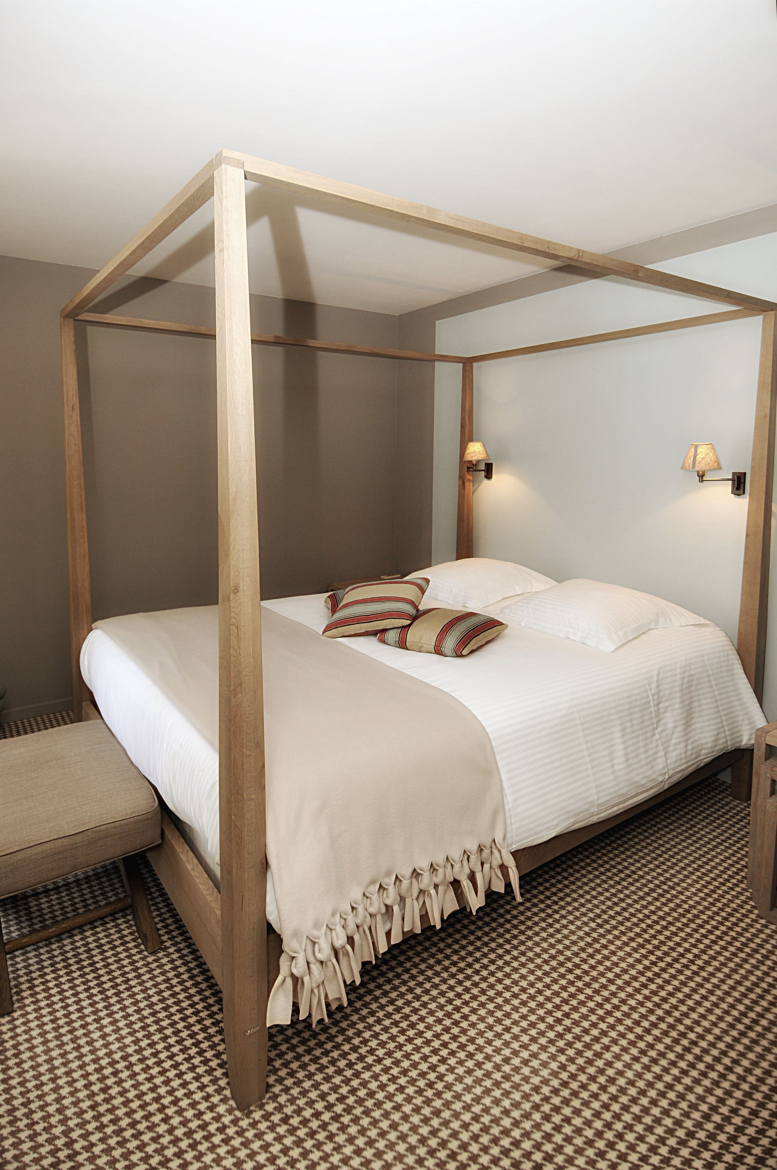 Uma cama de dossel com estrutura de madeira, roupa de cama branca e duas luminárias fixadas na parede.