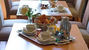 Una mesa con un desayuno: huevos, tostadas, jugo, una cafetera y un florero con flores.