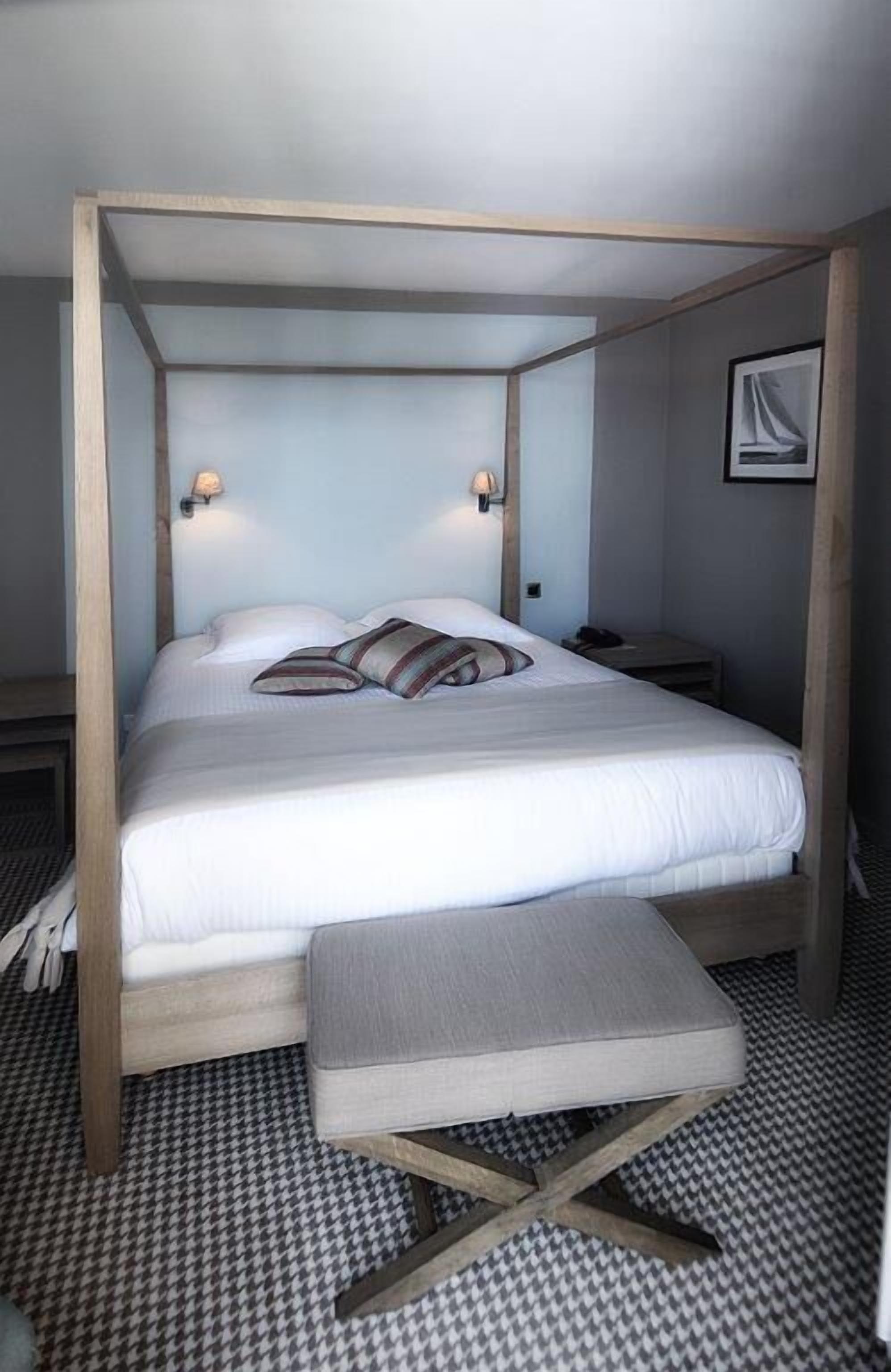 Een bed met houten frame, witte beddengoed en een bank aan het voeteneinde.