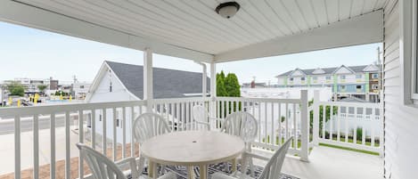 A covered balcony with a white railing, a round table, and four white chairs.