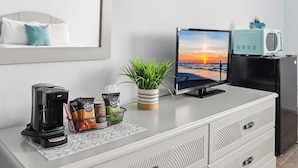 Une petite cuisine moderne équipée d’une machine à café, de capsules de café, d’une plante et d’un téléviseur diffusant une vue sur un coucher de soleil.