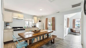 Une cuisine moderne avec des meubles blancs, une table à manger en bois et une cuisinière intégrée.