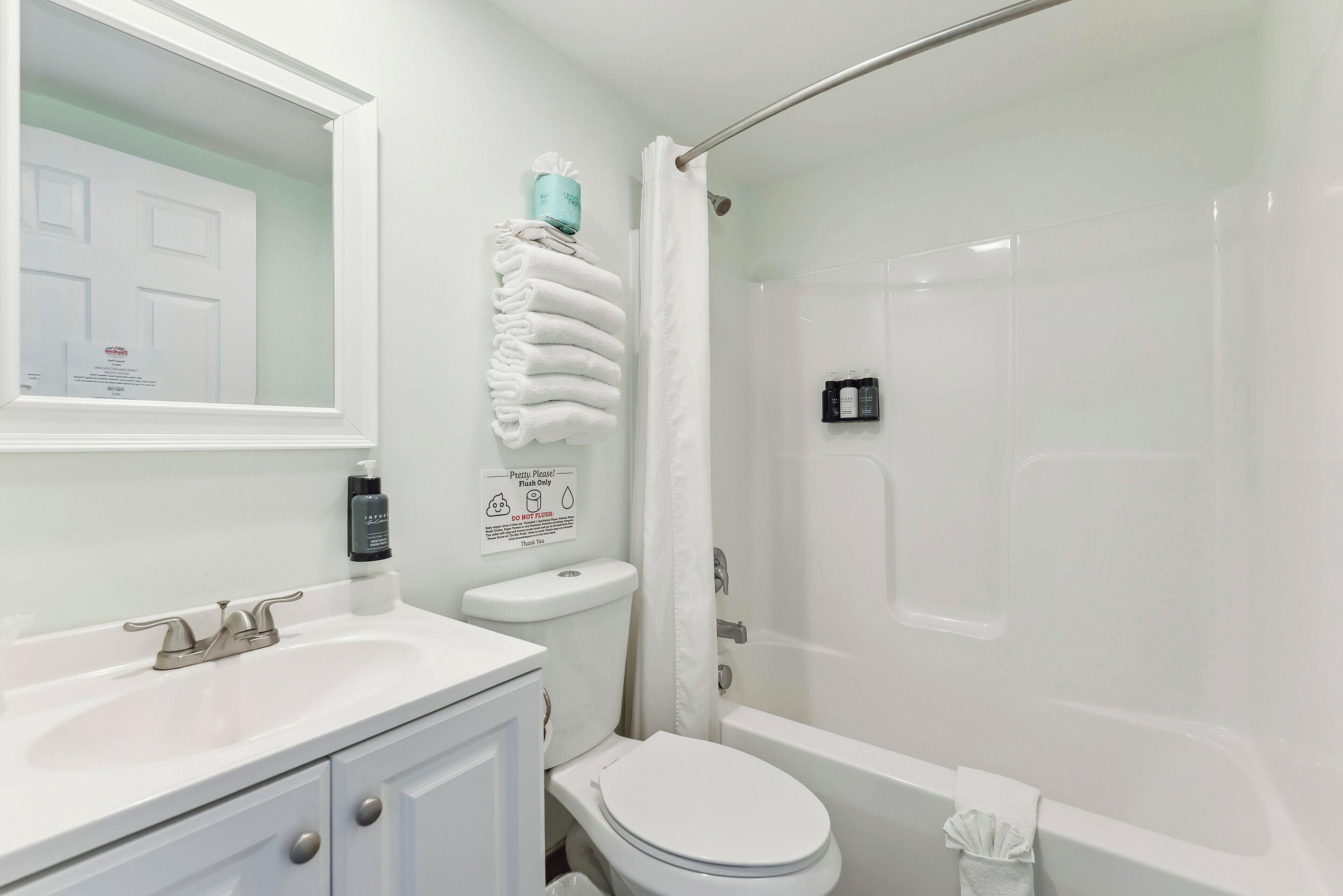 A bathroom with a white sink, toilet, and bathtub. There is a towel rack with folded towels and a sign on the wall.