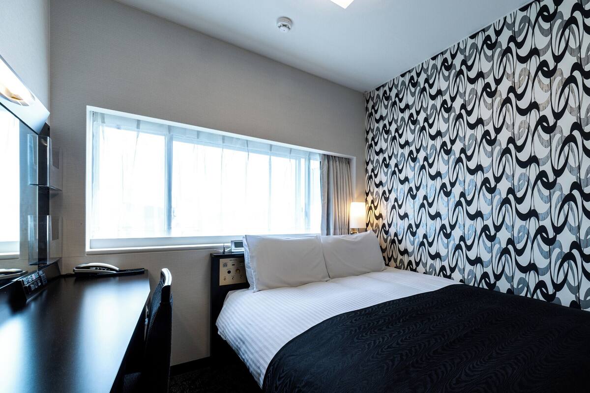 Een hotelkamer met een bed, een bureau, een telefoon en een raam met gordijnen.