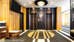 A modern lobby with a central chandelier, two elevators, and a patterned carpet. - APA Hotel Nagasaki Dejima (Nagasaki)