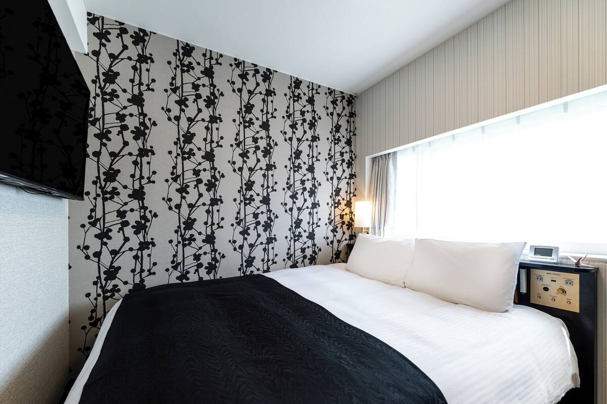 Een hotelkamer met een bed, nachtkastje, lamp en raam met gordijnen.