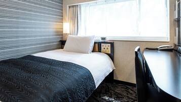 A hotel room with a bed, a desk, a lamp, and a window.