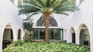 A spacious atrium with a central palm tree surrounded by lush greenery, white walls, and arched doorways leading to various rooms. - Park Club Europe - All Inclusive (Arona)