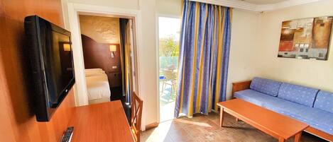 A hotel room with a bed, a TV, a ceiling fan, a sofa, and a table.