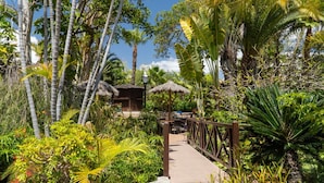 A pathway leading to a thatched-roof structure surrounded by lush tropical vegetation. - Park Club Europe - All Inclusive (Arona)