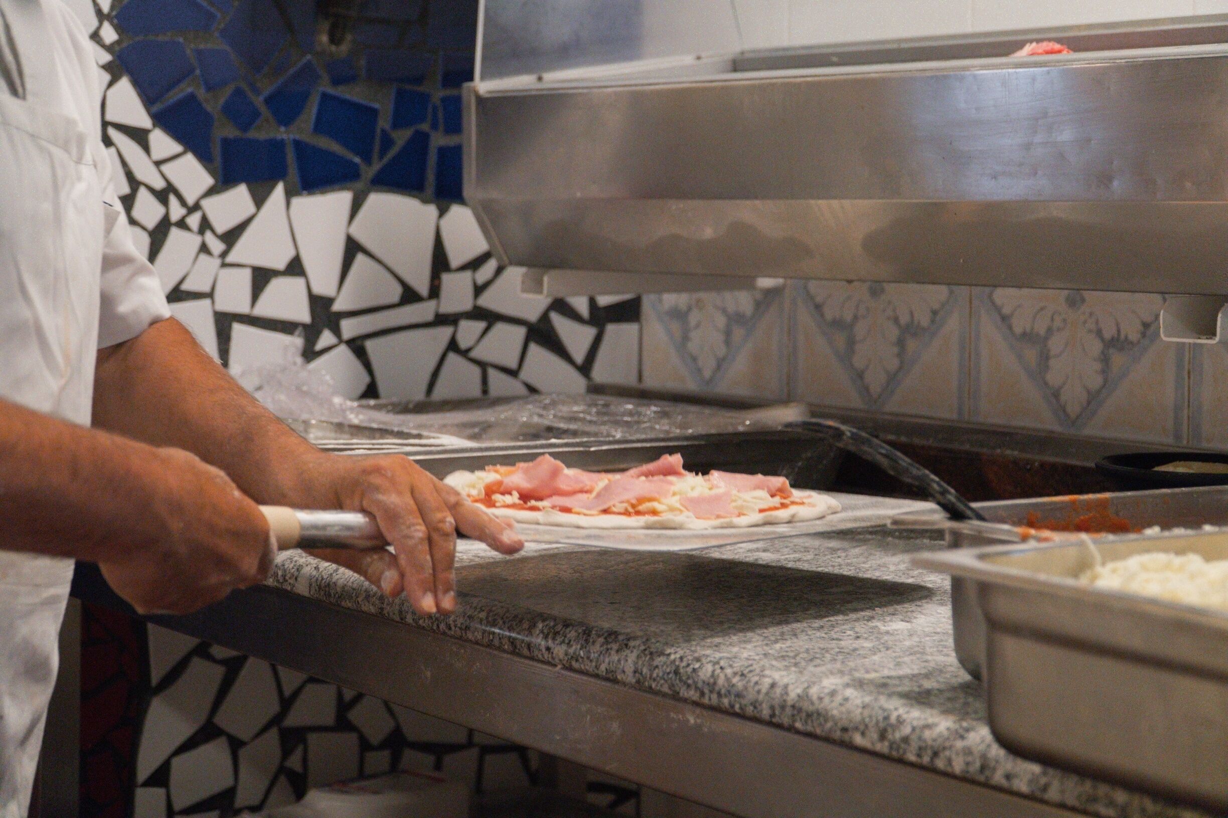 Un comptoir de cuisine où une personne prépare des aliments, avec un pare-feu en carreaux et un appareil en métal.
