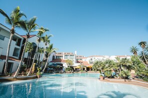 A resort pool area with palm trees, a bar, and multiple buildings in the background. - Park Club Europe - All Inclusive (Arona)