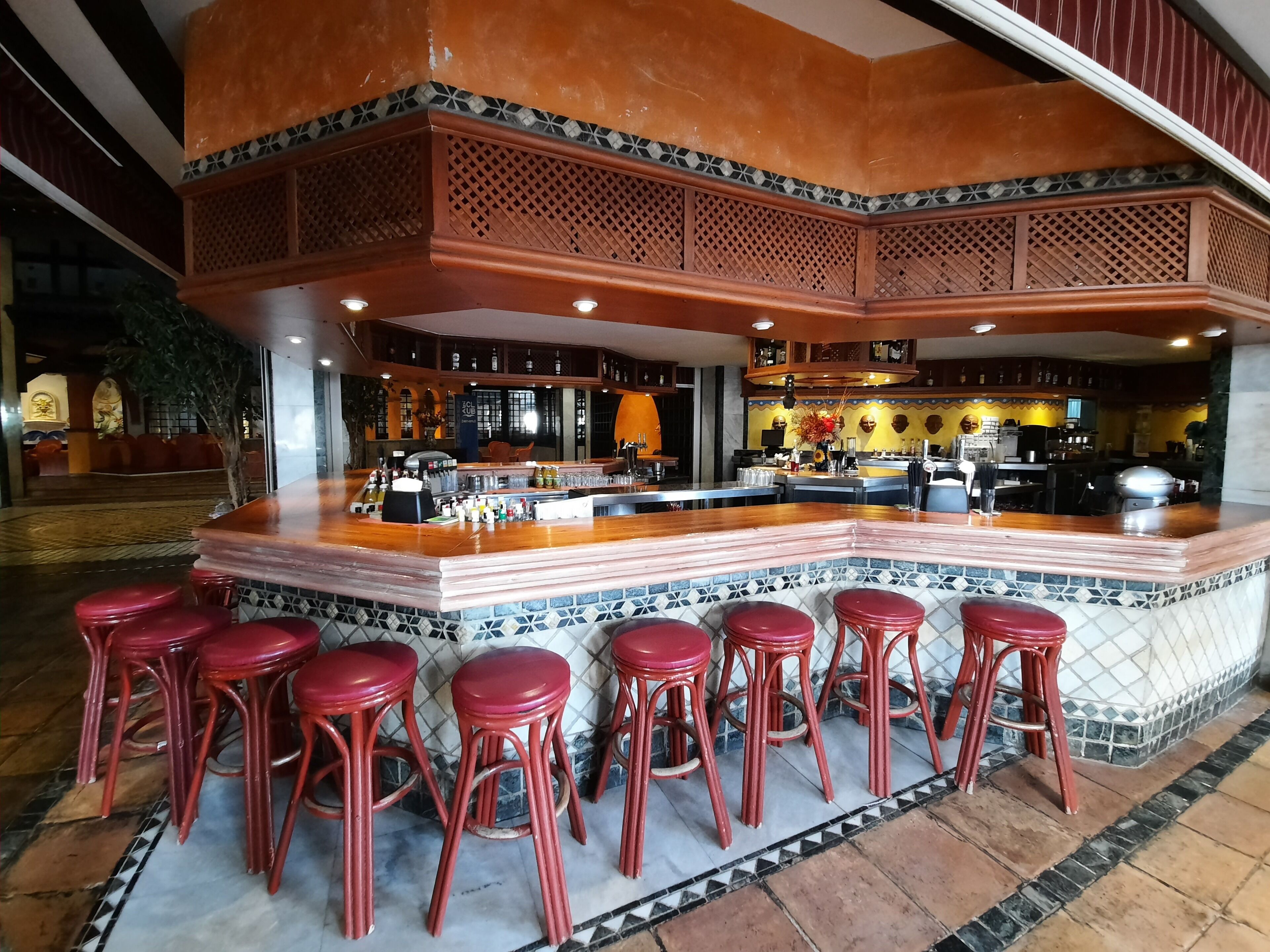 Zona de bar con una isla central, varios taburetes y un revoque de azulejos.